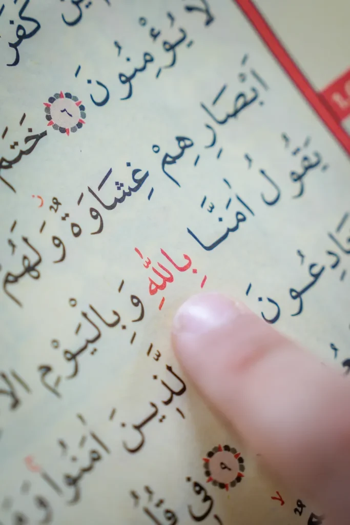 Finger following Arabic words on a Quran page