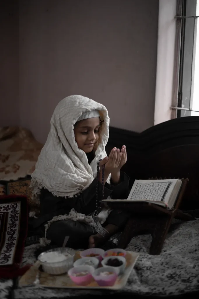 Girl in a hijab making dua with a Quran beside her