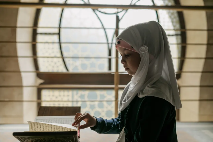 Girl in a hijab reading the Quran on a stand