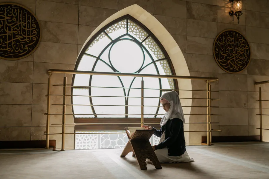 Girl reading the Quran by a mosque window