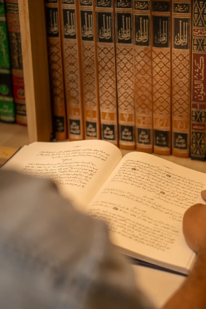 Open Arabic book held in front of shelves of Islamic books