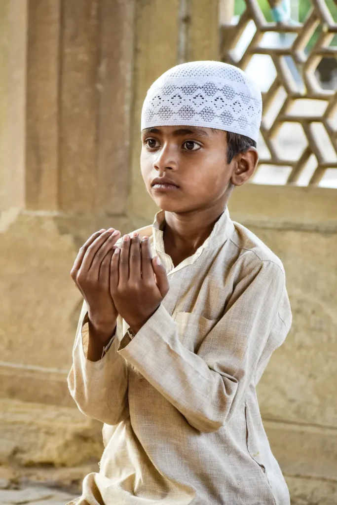 Boy in a kufi raising his hands to make dua