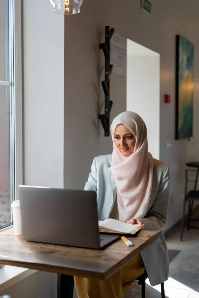 Woman in a hijab smiling during an online class on her laptop