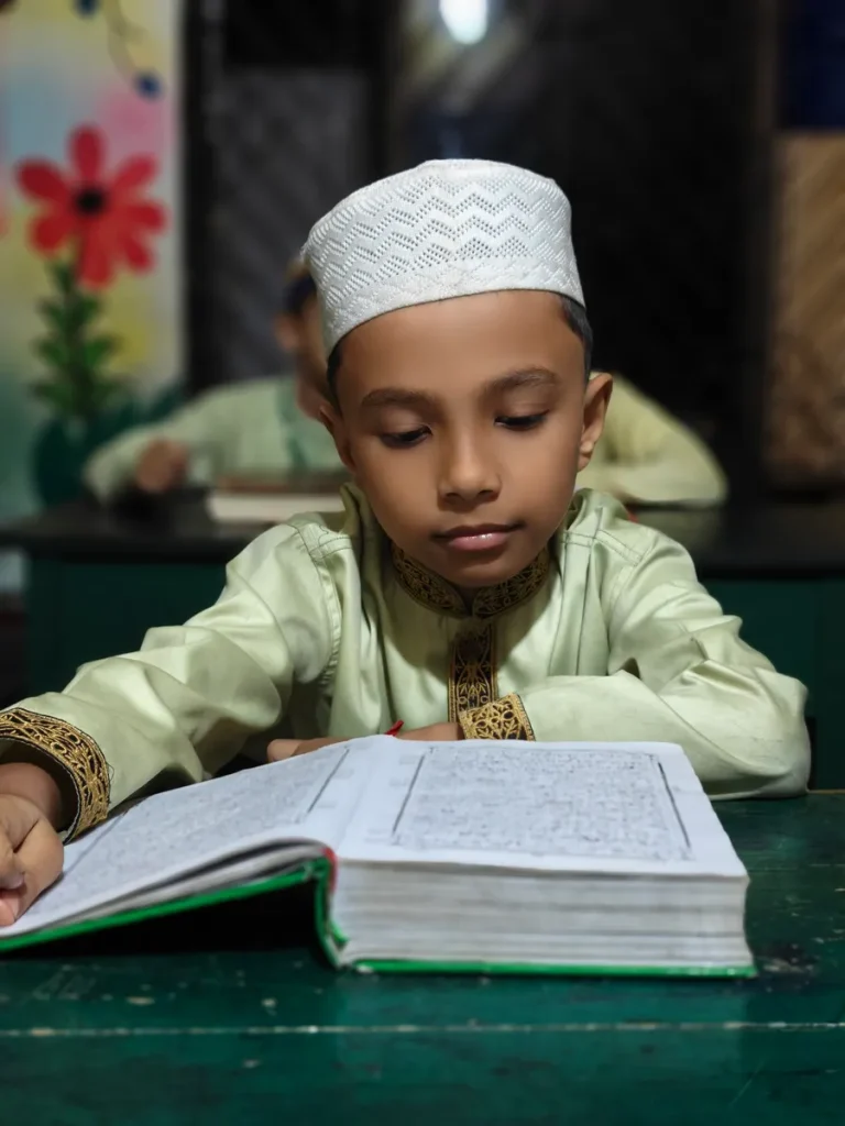 Boy in a kufi reading the Quran at his desk to memorize it