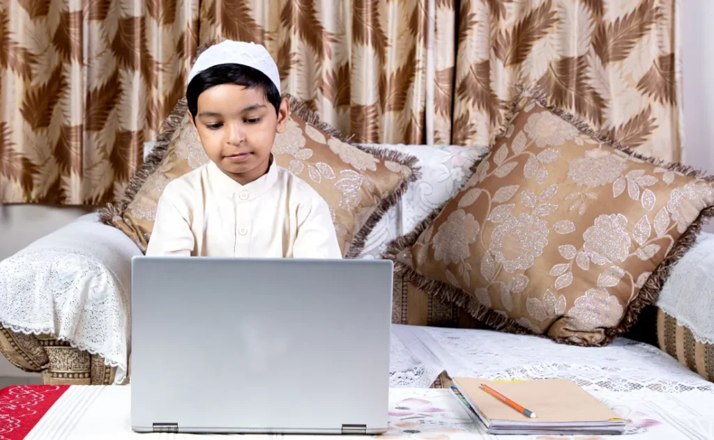 Boy in a kufi learning the Quran online on a laptop