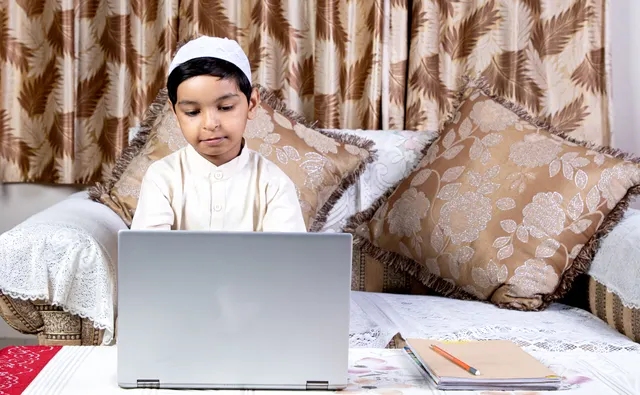 Boy in a kufi taking an online Quran class on a laptop