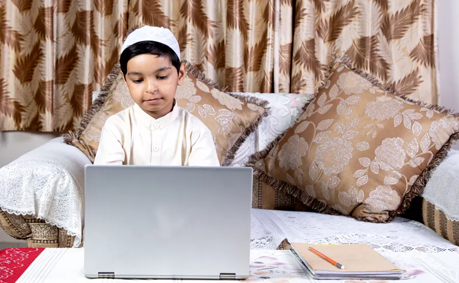 Boy in a kufi taking an online Quran class on a laptop