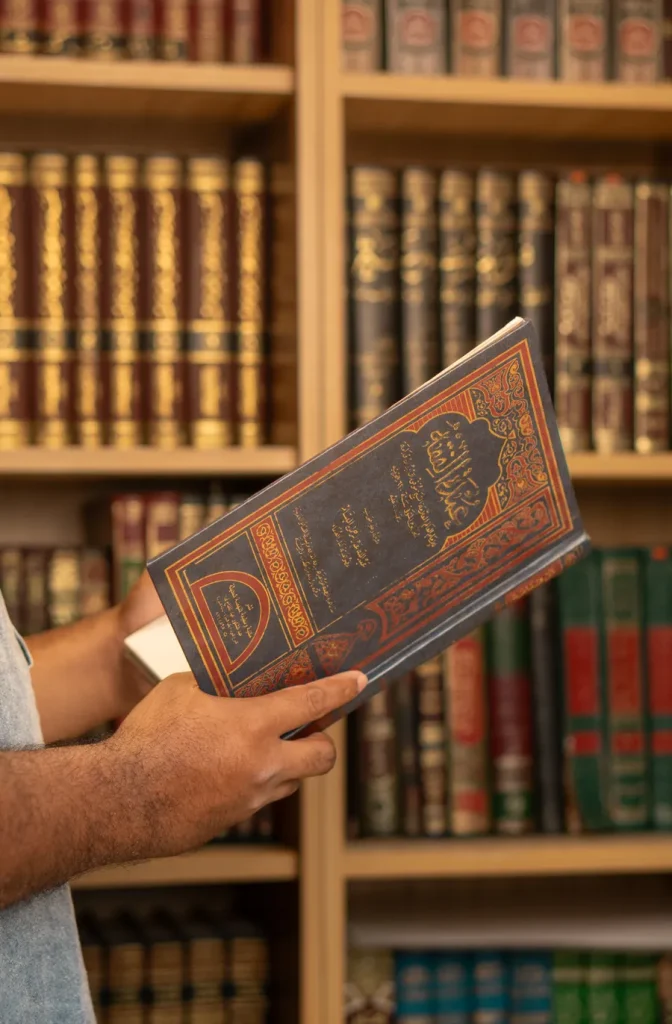 Student holding an Arabic Islamic book in a library