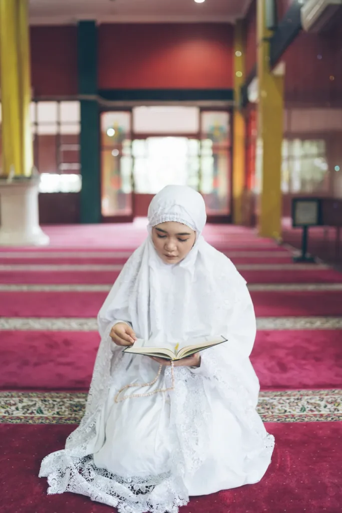 Woman in a white hijab reading the Quran in a mosque