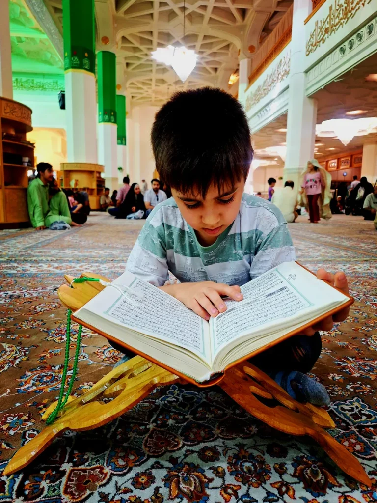 Boy reading the Quran from a Mushaf on a wooden stand
