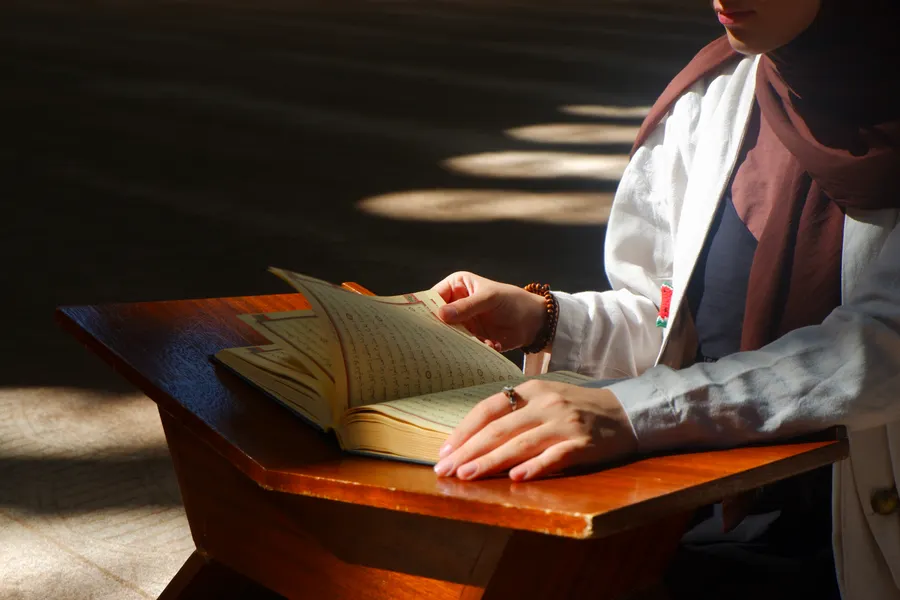 Hands resting on a Quran open on a wooden stand