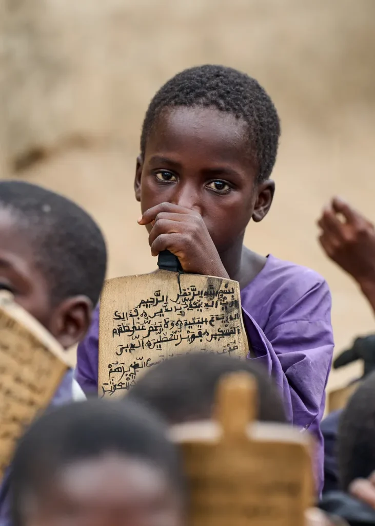 Child holding a wooden tablet with Arabic writing